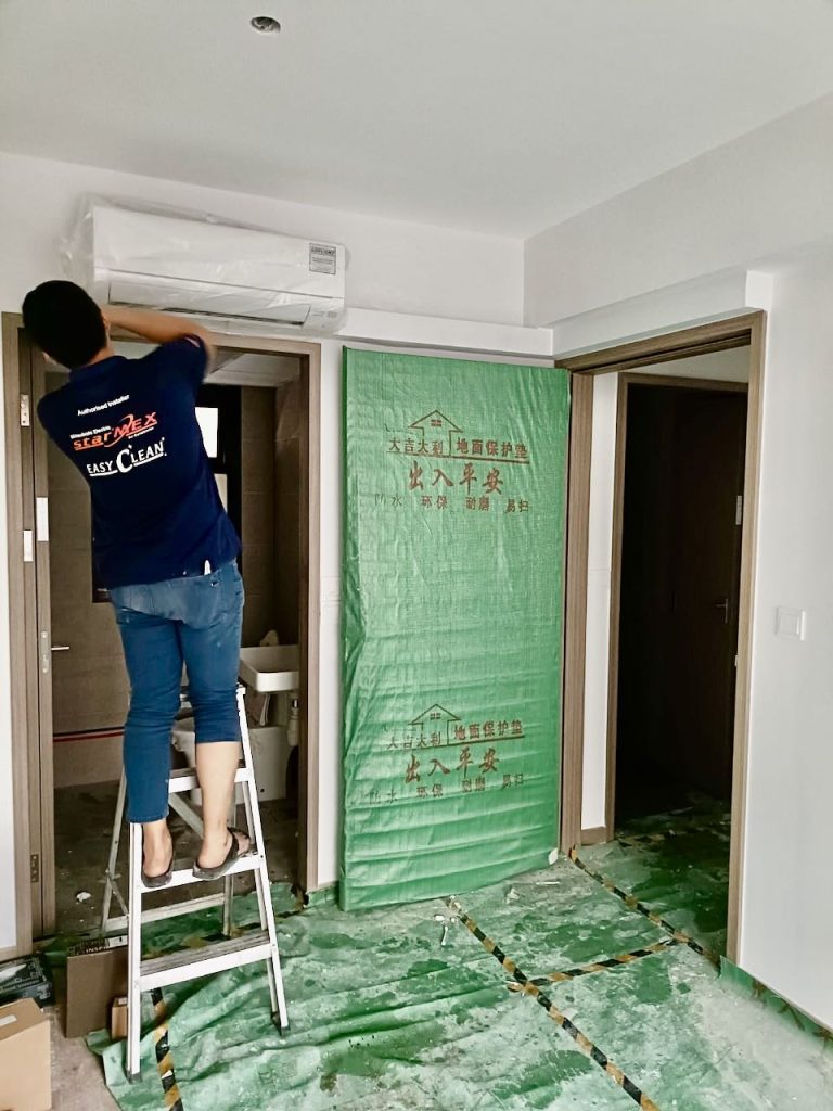 Technician installing a Mitsubishi Starmex air conditioner in a modern Singapore home.